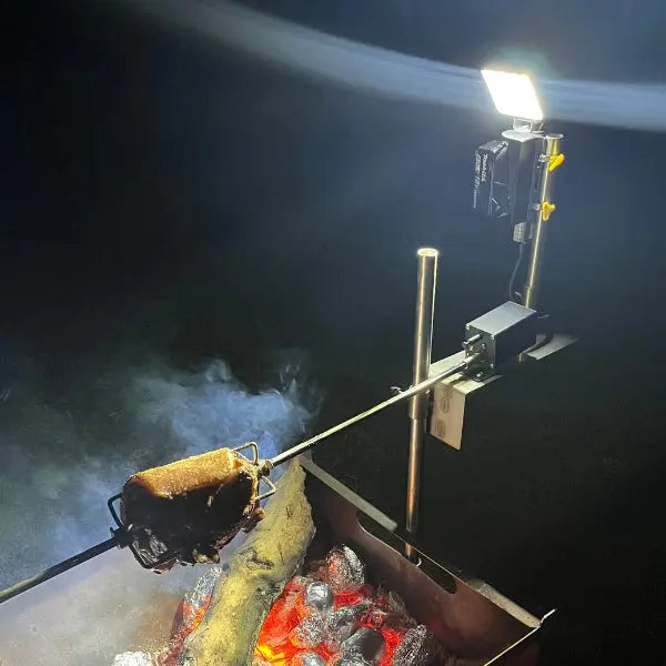 Power Plate light on a pole lighting a campfire rotisserie at night